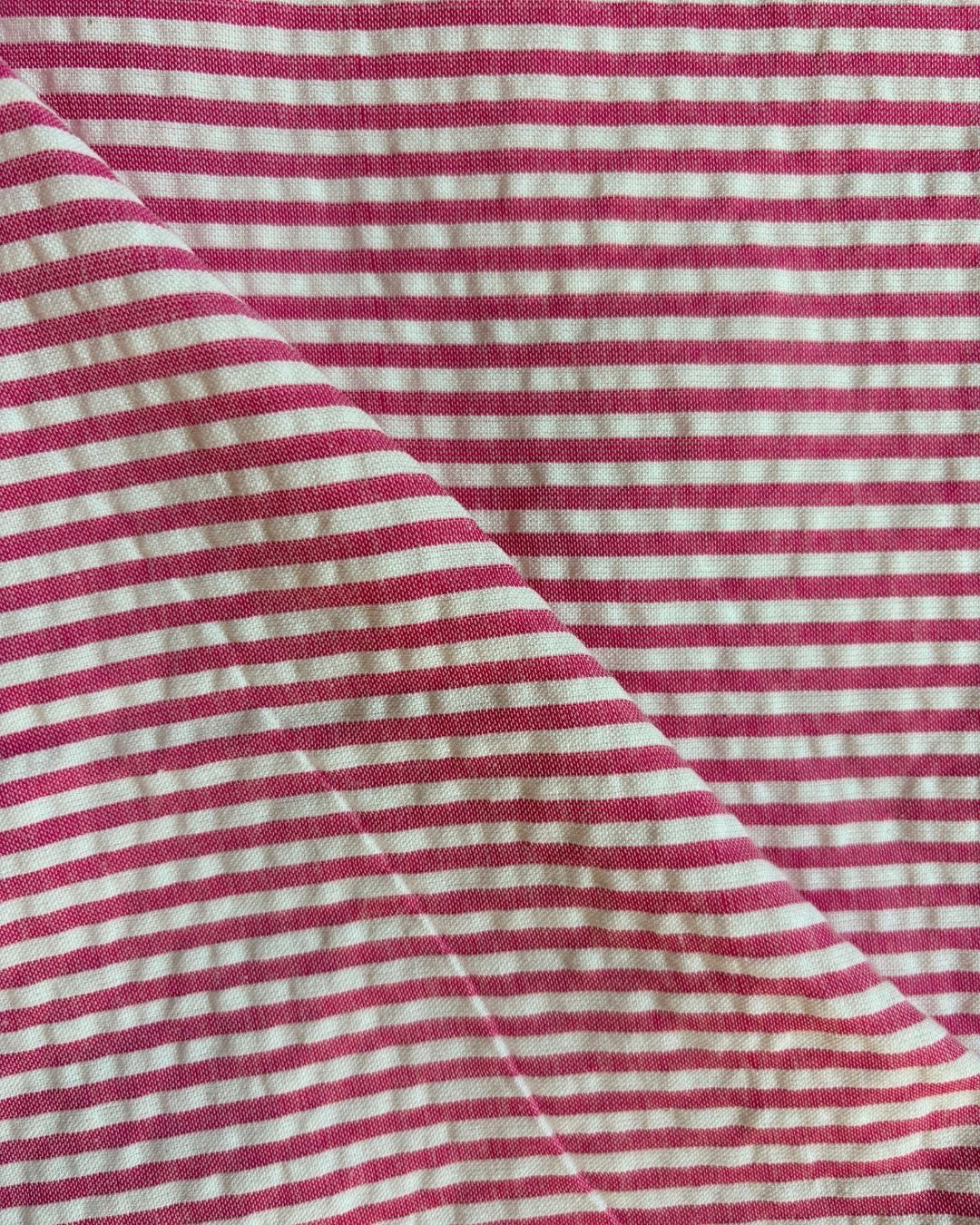 A close-up of a pink and white striped fabric with a visible diagonal fold showing the texture and weave.
