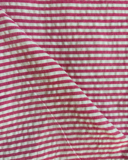 A close-up of a pink and white striped fabric with a visible diagonal fold showing the texture and weave.